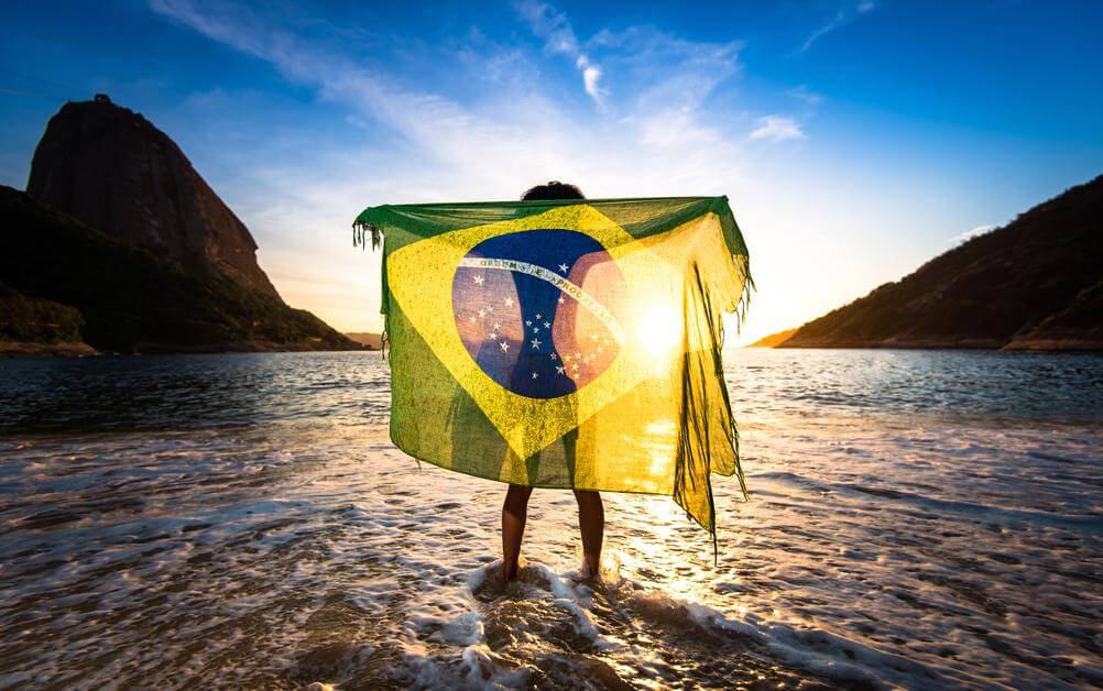 A man holding the flag of Brazil, representing Lotofacil on the beach!