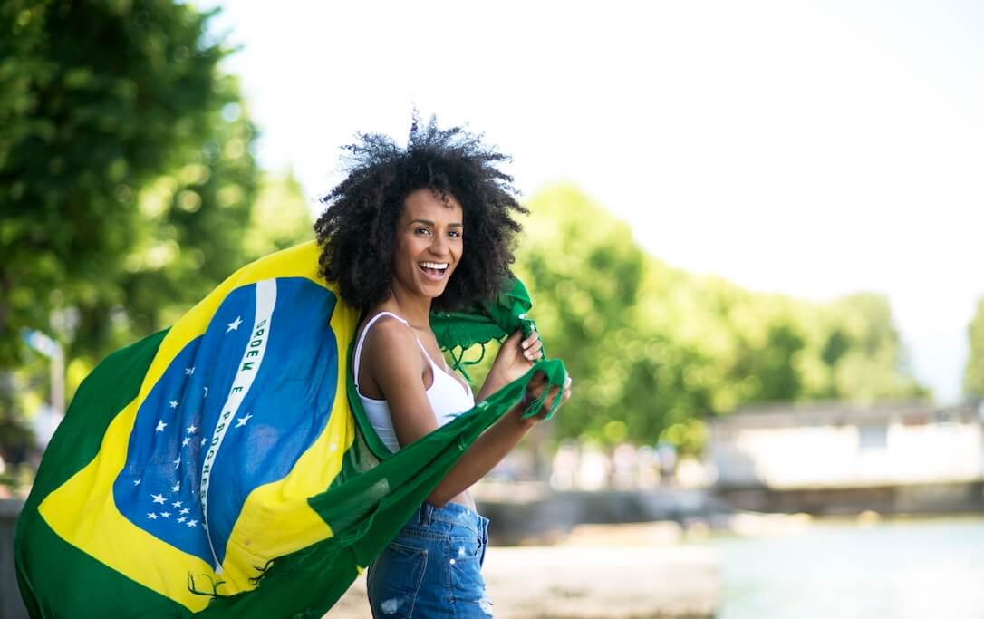 A woman on a beach with a Brazil flag draped over her shoulders, happy to bet on Quina during the day