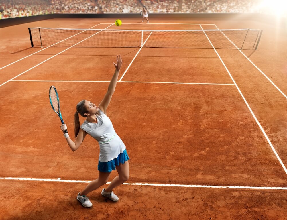 A tennis players tossing the ball in the air for a serve on a clay court