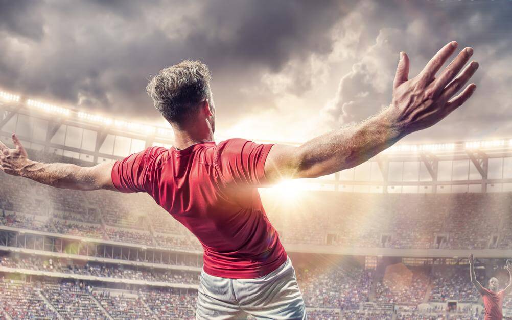 A footballer in a red jersey celebrating with his back to camera having scored a goal - good news for those who placed a both teams to score bet!